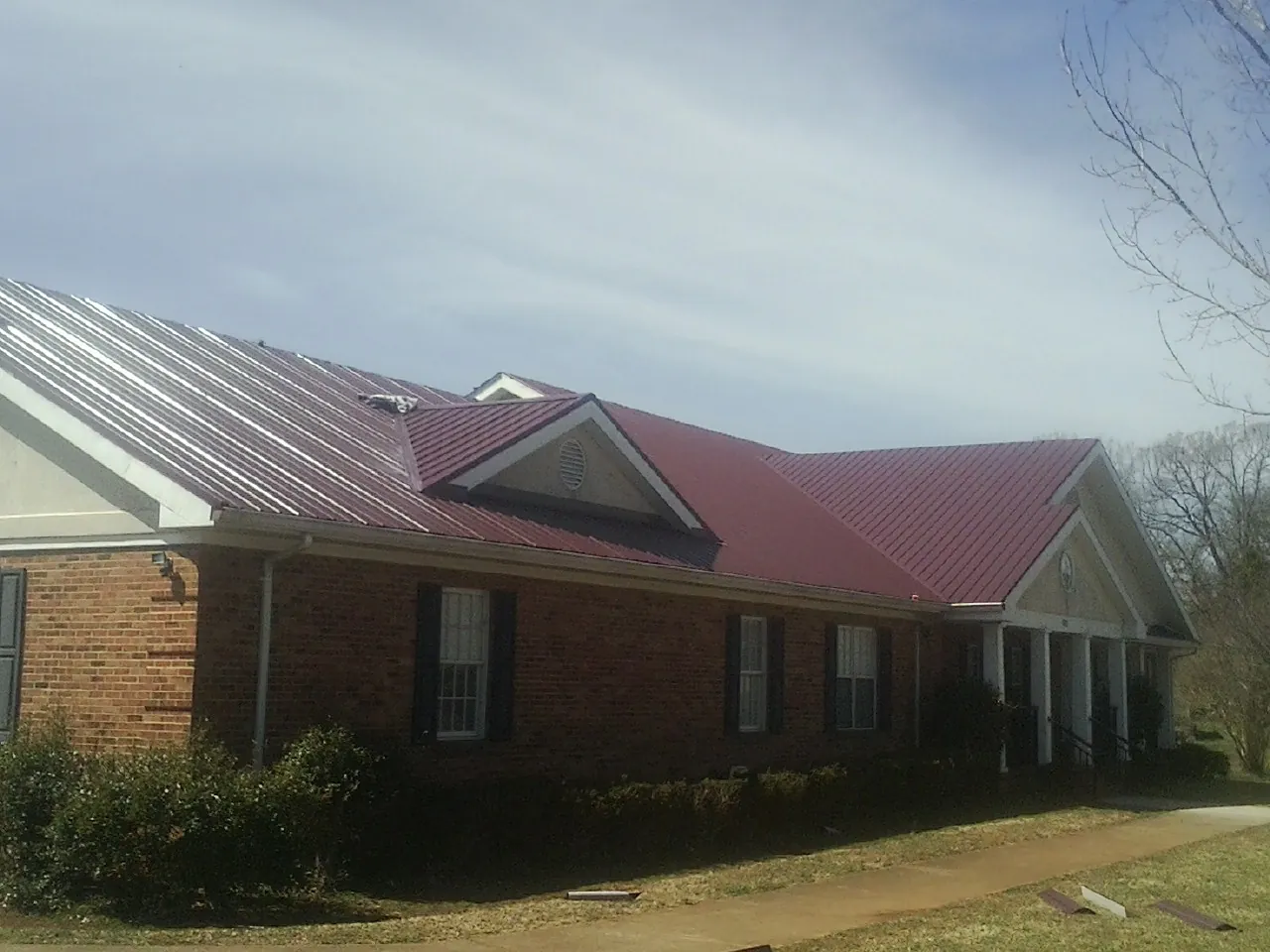 Red metal roof with gabled entries on a long brick building, from a Hail Damage Roof Repair job in Bergheim