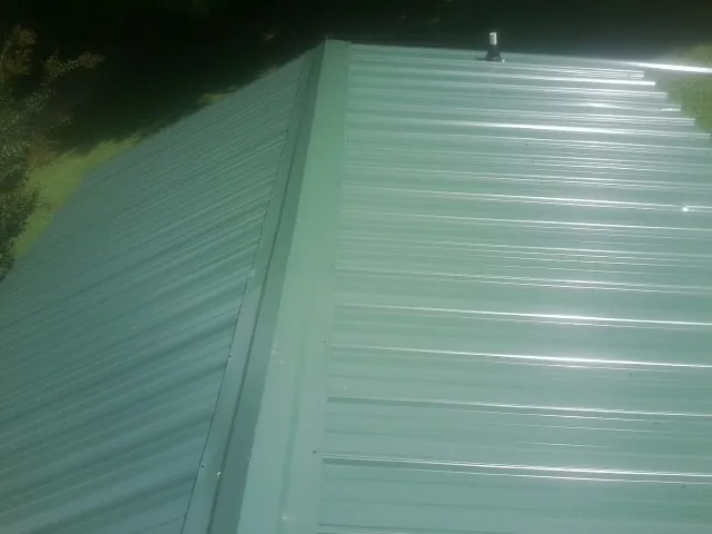 New green metal panels meeting at the ridge of a roof — Flat Roof Repair work by our crew in Bergheim